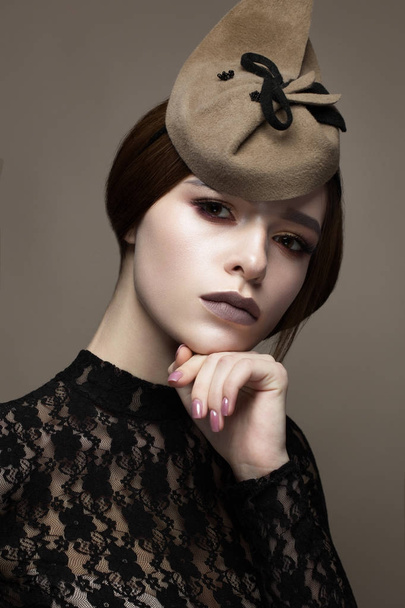 A young girl in an unusual hat and an elegant hairdo. Beautiful model with a gentle make-up in chocolate shades. Retro image. Beauty of the face. Photo taken in the studio. - Foto, Imagen