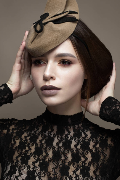 A young girl in an unusual hat and an elegant hairdo. Beautiful model with a gentle make-up in chocolate shades. Retro image. Beauty of the face. Photo taken in the studio. - Foto, immagini
