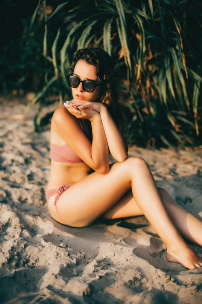 Mooie Kaukasische vrouw in sexy zwembroek op het strand op de zonsondergang zonlicht, sexy meisje, vrouw op vakantie, zonsondergang aan zee, palmen op het strand - Foto, afbeelding