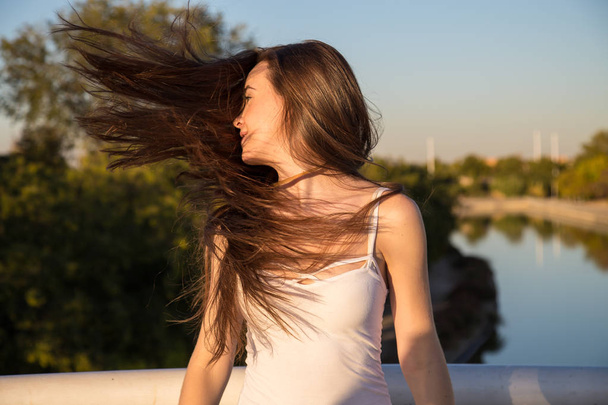 Pretty young woman shaking hair in sunny park on the background of artificial river.   - Photo, image
