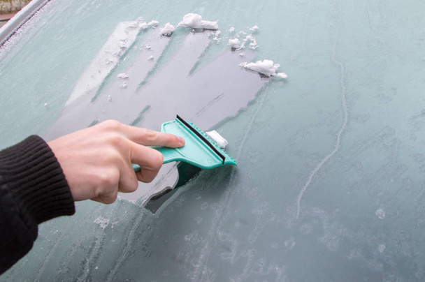Mies puhdistaa jäätynyttä auton ikkunaa jääkaapimella
. - Valokuva, kuva