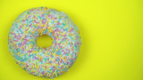 Heerlijke zoete donut draaien op een plaat. Bovenaanzicht. Helder en kleurrijk bestrooid donut close-up macro geschoten spinnen op een gele achtergrond. - Video