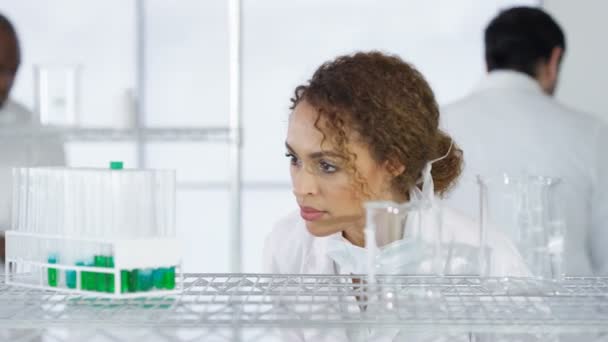 4K Research scientist in white coat working in lab with colleagues in background - Footage, Video