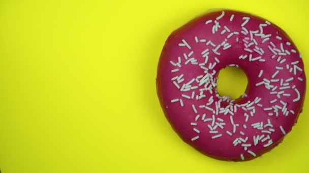 Delicious sweet donut rotating on a plate. Top view. Bright and colorful sprinkled donut close-up macro shot spinning on a yellow background. - Footage, Video
