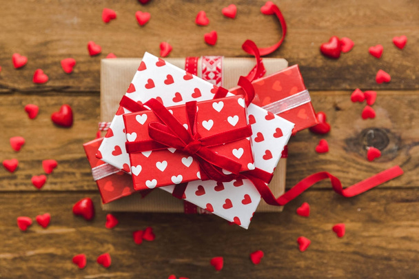 Stack of handcrafted gift boxes  with red bow ribbon and hearts on wooden table for Valentines day - Fotoğraf, Görsel