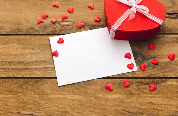 Blank valentines greeting card and small red gift box on wooden table - Fotoğraf, Görsel