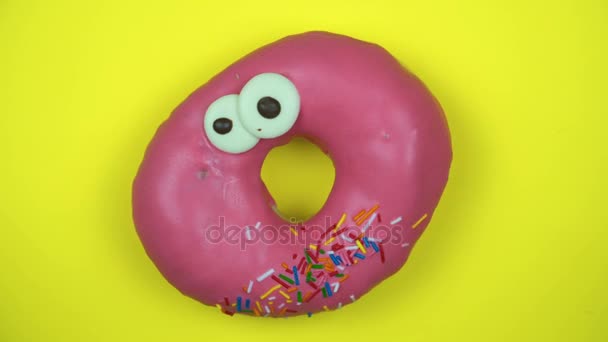 Delicious sweet donut rotating on a plate. Top view. Bright and colorful sprinkled donut close-up macro shot spinning on a yellow background. - Footage, Video