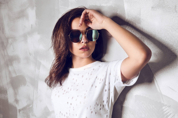 Wwoman in round sunglasses posing near a gray wall at studio - Фото, зображення