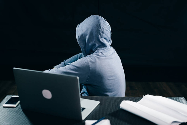 Salaperäinen mies piilottaa kasvonsa konepellin alle, istuu kannettavan vieressä, hakkeri
 - Valokuva, kuva
