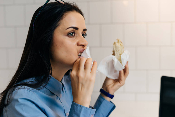 young brunette girl in blue shirt eating a sandwich in cafe - Fotó, kép