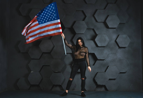 beautiful girl posing in studio with american flag on gray background in black clothes - Foto, afbeelding
