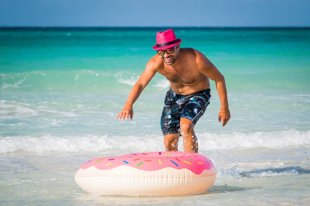 Happy handsome smiling man in pink hat is running to big inflata - Фото, изображение
