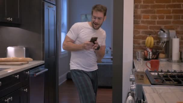 Man in his pajamas dancing and checking his notifications on his smart phone - Materiał filmowy, wideo