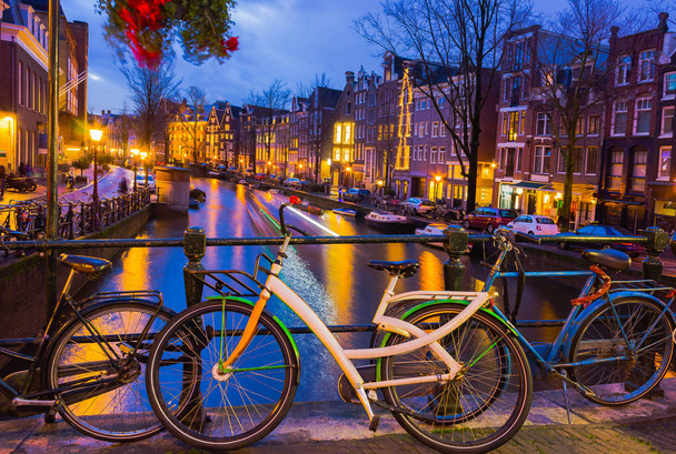 Iluminación nocturna del canal y puente de Ámsterdam con casas holandesas típicas, barcos y bicicletas
. - Foto, imagen