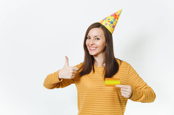 Beautiful caucasian lucky fun young happy woman in yellow clothes, birthday party hat holding golden credit card, celebrating holiday, showing thumb up on white background isolated for advertisement. - Photo, Image