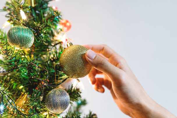 Hand hanging sparkling golden Christmas balls on Christmas tree for decorating in Holiday - Foto, afbeelding