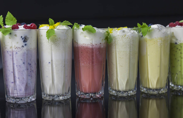 glasses of various milkshakes (chocolate, strawberry and vanilla, kiwi, blueberry) on black background - Фото, изображение