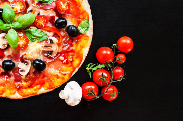 Hot pizza with Pepperoni Sausage on a dark background  with copy space. Pizza with mushrooms, tomatoes, cheese, onion, oil, pepper, salt, basil, olive - Photo, image