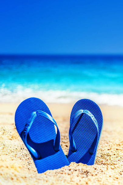 Summer fun time and accessories on a sand on the beach. Blue  sandal flip flop on the white sand with blue sea and sky in summer vacations, copy space - Foto, Imagen