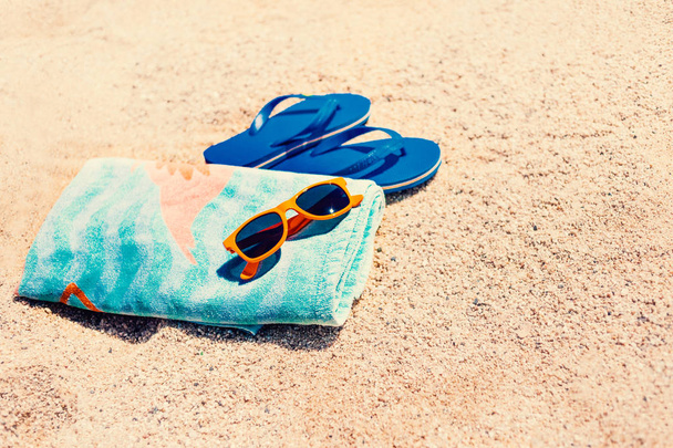Blue  sandal flip flop,  sunglasses and towel  on yellow sand. Summer fun time and accessories on the beach,  summer vacations, copy space - Fotoğraf, Görsel