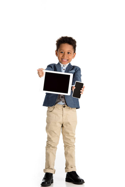 smiling african american kid showing tablet and smartphone on white  - Фото, изображение