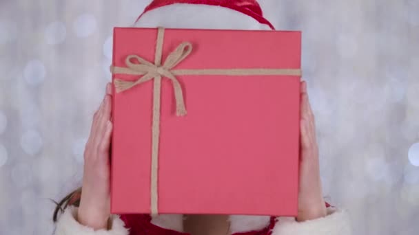 Santa woman jelmezben tart egy ajándék a lány kezét, és a hullámok a kezét, hello. Bokeh háttér. Közelről - Felvétel, videó