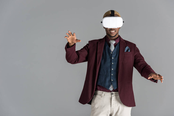 Afrika kökenli Amerikalı adam gri arka plan üzerinde uzanmış kollu VR gözlük kullanma     - Fotoğraf, Görsel