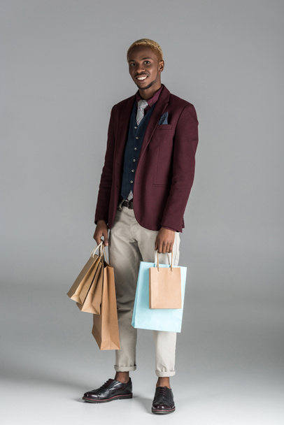 Αφρικανική άνθρωπος με χαρτί ψώνια σακούλες στα χέρια σε γκρίζο φόντο   - Φωτογραφία, εικόνα