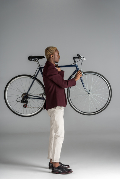 Αφρικανική αμερικανική άνθρωπος που κρατά ποδήλατο στα χέρια σε γκρίζο φόντο - Φωτογραφία, εικόνα