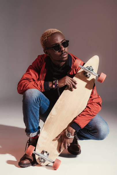 young fashionable african american skateboarder sitting and holding longboard - Photo, Image