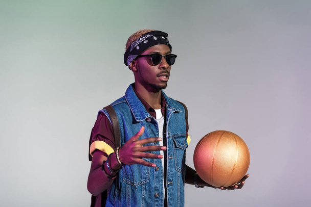 stylish young african american man holding golden basketball ball isolated on grey - Zdjęcie, obraz