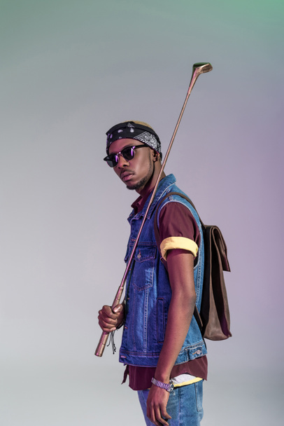 stylish young african american man holding golden golf club and looking at camera isolated on grey - Foto, afbeelding