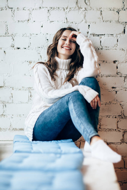woman laughing while sitting on window sill on cushion at home - Foto, Bild