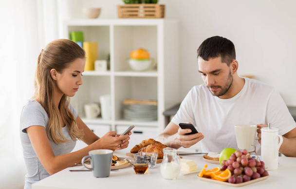 couple with smartphones having breakfast at home - 写真・画像