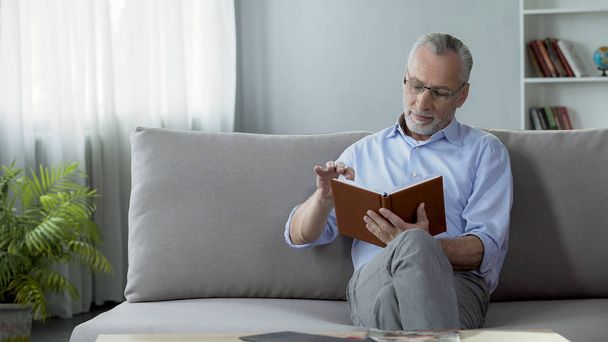 Happy old man sitting on couch and reading weekend plan, hobby and free time - 写真・画像