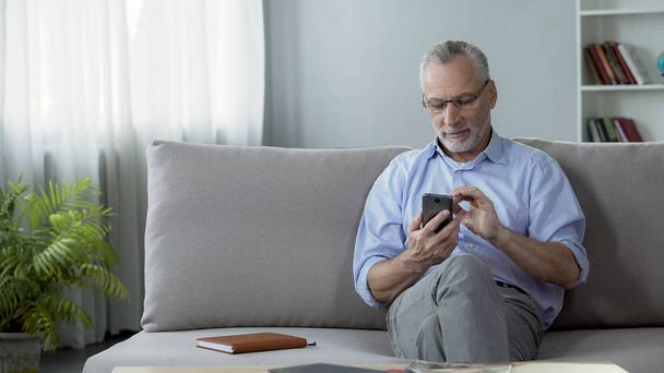 Kind senior man typing telephone number on cellphone, modern technologies - Фото, изображение