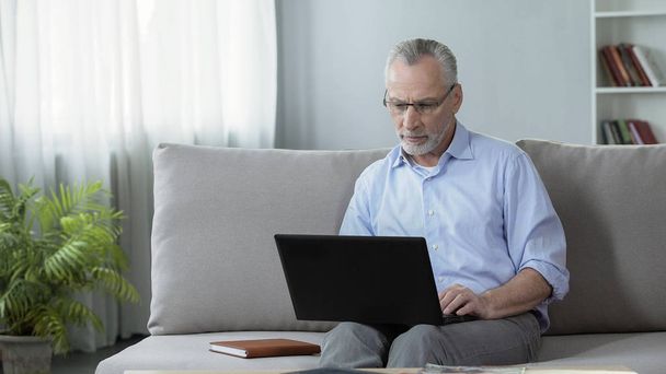 Male journalist sitting on couch and working on laptop, freelance and profession - Photo, Image