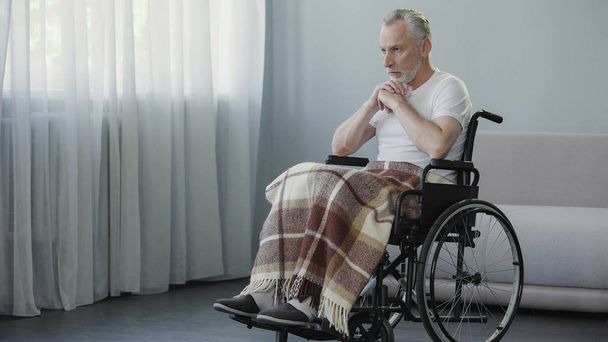 Old ill male sitting in wheelchair and praying, depression and terrible disease - Foto, afbeelding