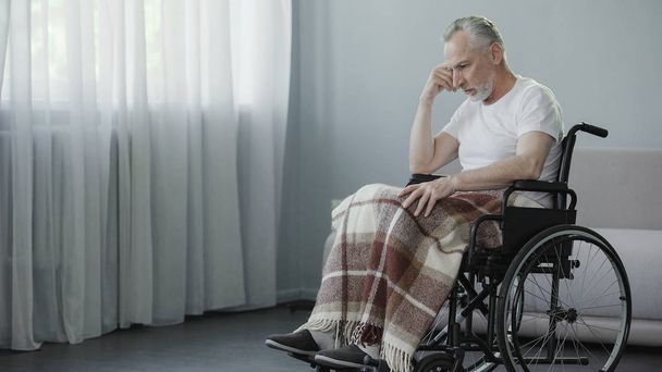 Man with disabilities sitting in wheelchair and thinking about illness, disease - Foto, afbeelding