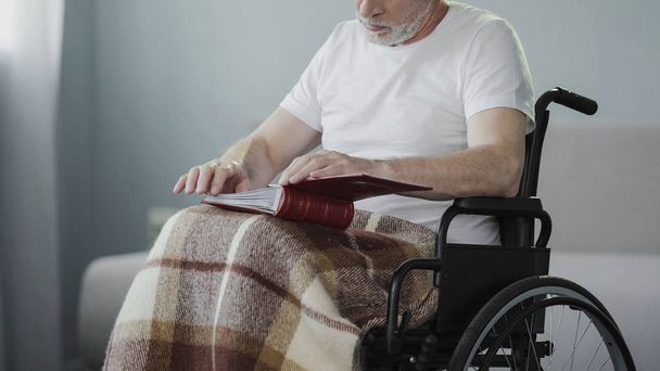 Paralyzed senior male reviewing album with photos, missing his family support - Foto, Bild