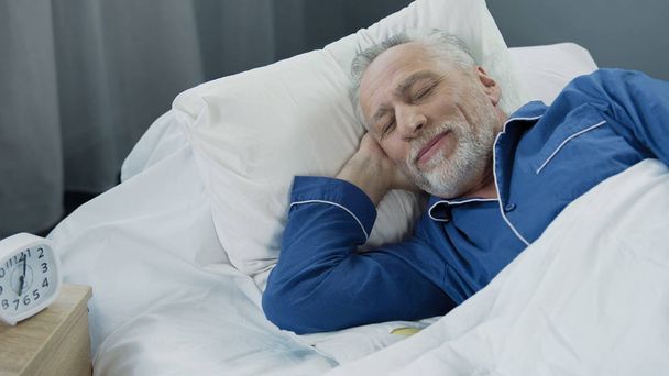 Senior man smiling while asleep in the morning, pleased pensioner lying in bed - Фото, зображення