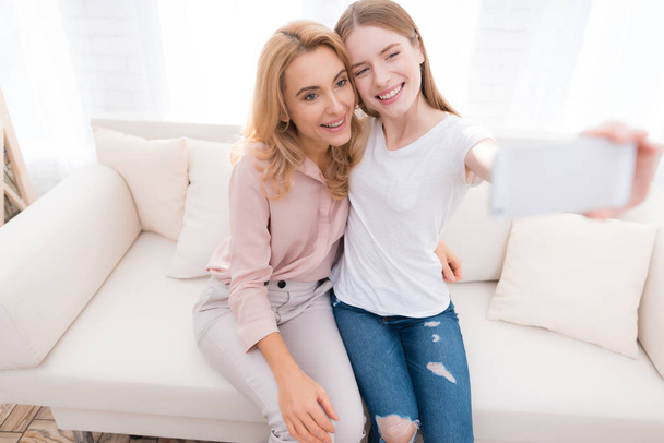 Mom and teenage daughter do selfie. They are sitting on the couch at home. They are in a good mood. They are happy with each other. - Φωτογραφία, εικόνα