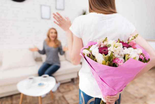 The daughter gives her mother flowers and gifts. She makes her a surprise. Mom is very surprised. They are together at home. - Photo, image