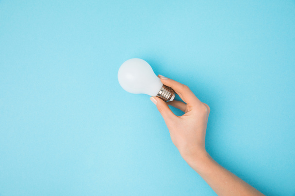 partial view of woman holding light bulb in hand isolated on blue - Foto, Imagen