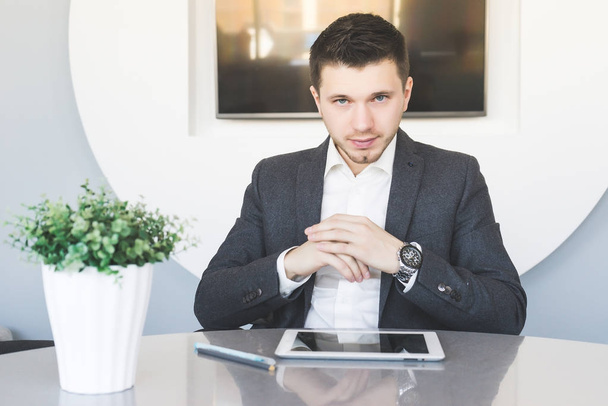 a young man in a business suit seriously sitting at a table - Foto, afbeelding