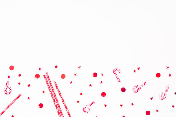 Concepto de año nuevo. Decoración de Navidad, bastones de caramelo y confeti rojo sobre fondo blanco. Piso tendido, vista superior
. - Foto, Imagen