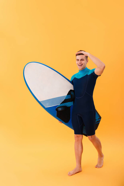 Full length image of Young smiling surfer walking with surfboard - 写真・画像