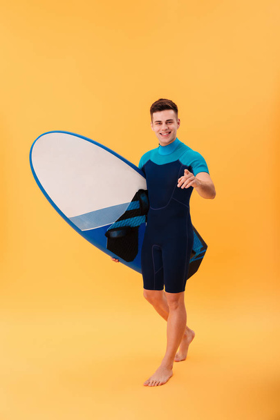 Full length image of smiling surfer walking with surfboard - Foto, Bild