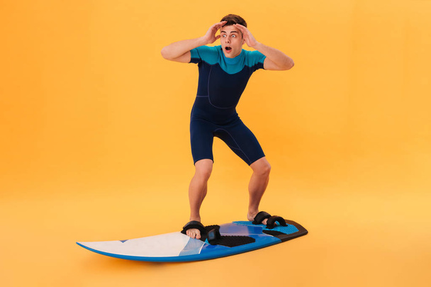 Picture of a Shocked surfer in wetsuit using surfboard - Zdjęcie, obraz