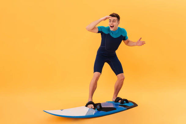 Image of Surprised happy surfer in wetsuit using surfboard - Photo, image